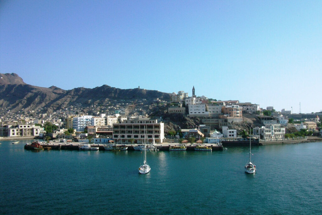 Durante o dia, um mar na frente e alguns barcos, atrás o porto com alguns prédios. Foto para ilustrar post sobre seguro viagem para o Iêmen.