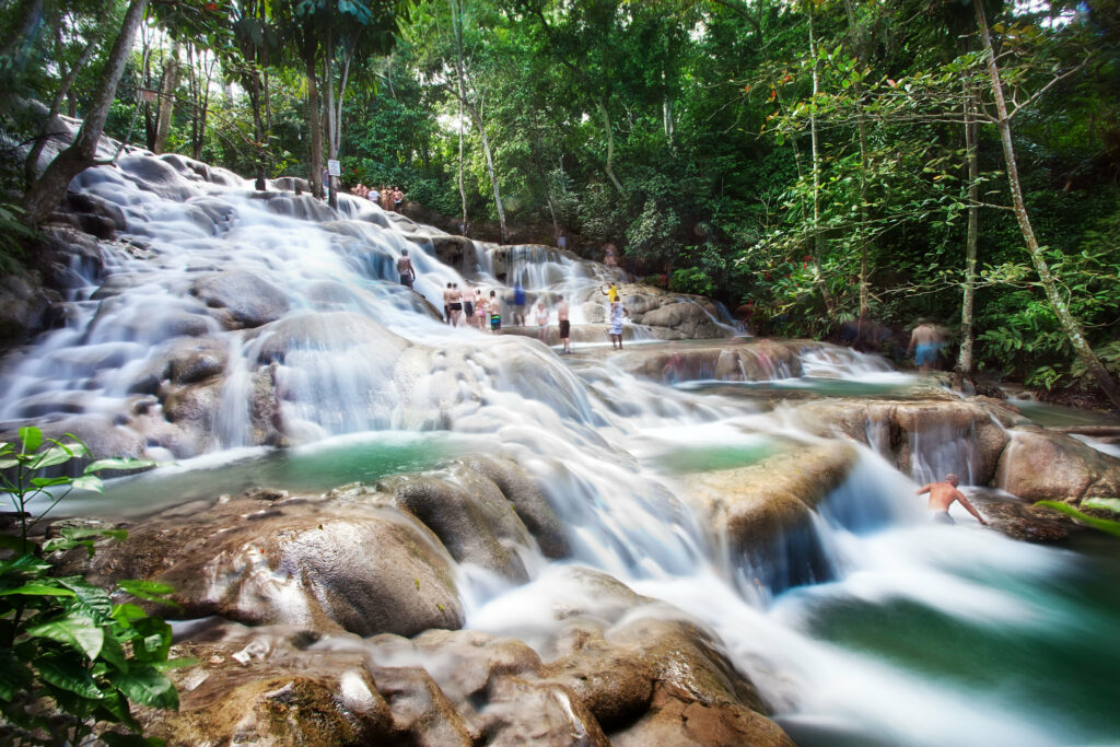 Pessoas em uma grande cachoeira rodeada por árvores. Foto para ilustrar post chip internacional para a Jamaica.