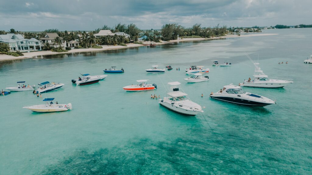 Foto tirada durante o dia de vários barcos no mar. Mais ao fundo é possível ver diversas casas e árvores. Imagem para ilustrar post chip internacional para as Ilhas Cayman.