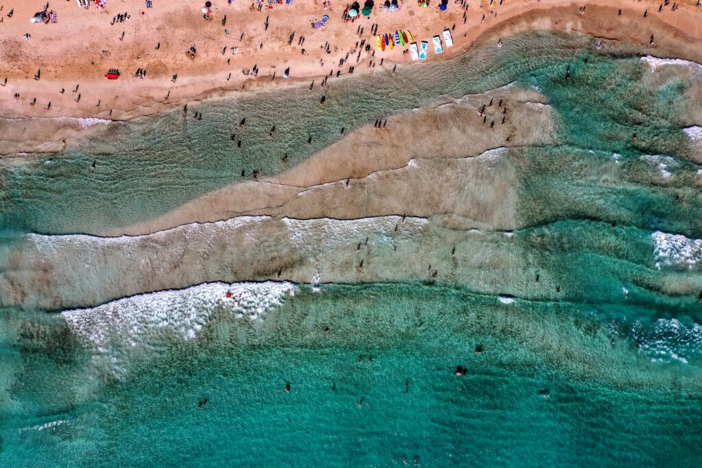 Foto aérea do mar quebrando em faixa de terra com banhistas para representar o chip internacional para o Líbano. 