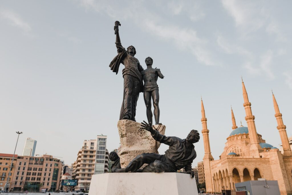 Foto de estátua preta com três homens, construção ao fundo e alguns prédios em dia nublado para representar o chip internacional para o Líbano. 