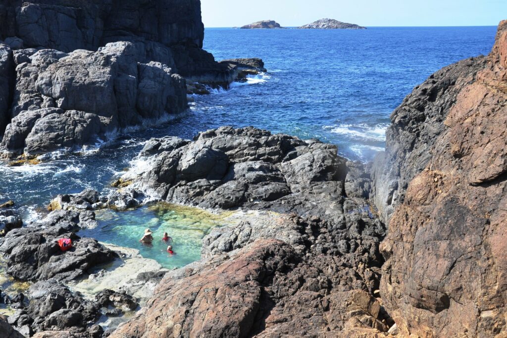 Três pessoas nadando em uma piscina natural, cercada por rochas em meio ao mar. Foto para ilustrar post de chip internacional para as Ilhas Virgens Espanholas.