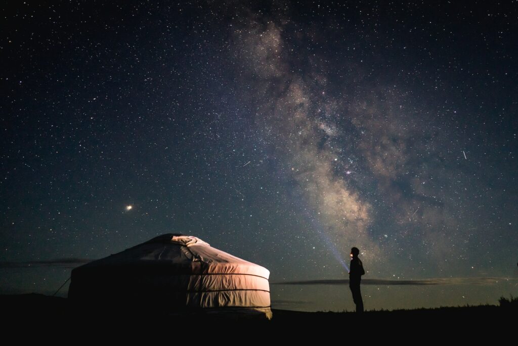 Homem em pé ao lado de uma tenda e olhando para o céu estrelado. Imagem para ilustrar post de chip internacional para a Mongólia.