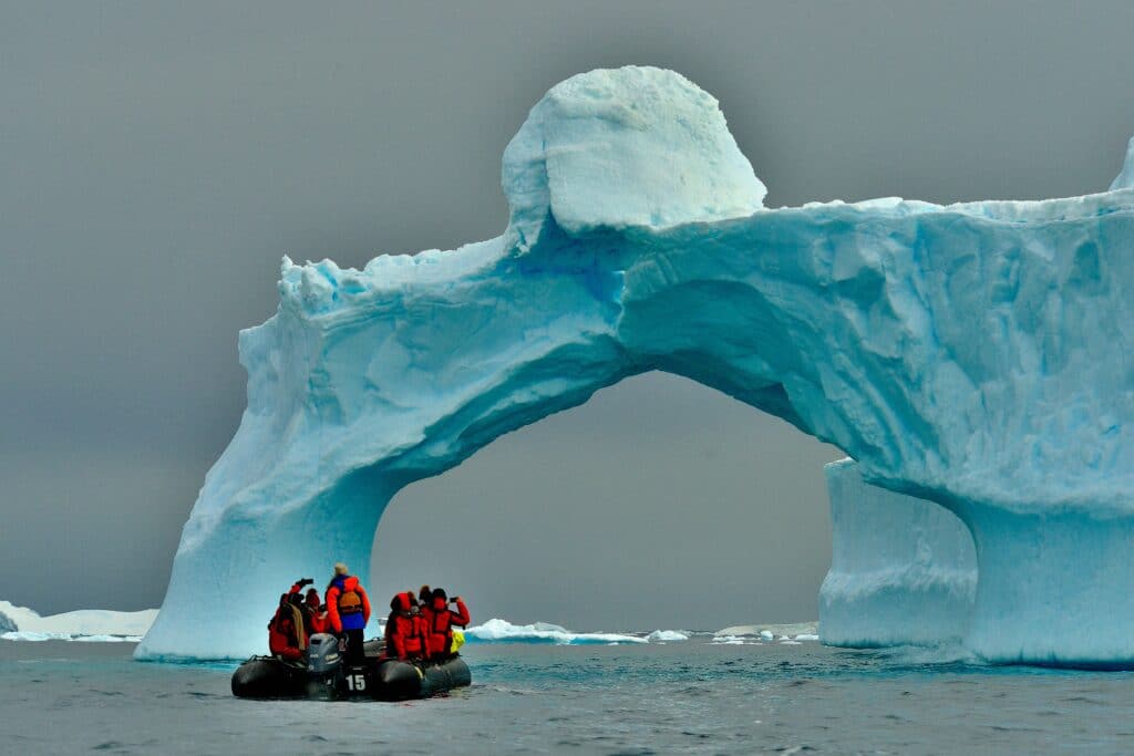 Durante o dia um grupo de pessoas dentro de um bote no mar da Antártida perto de uma rocha de gelo.