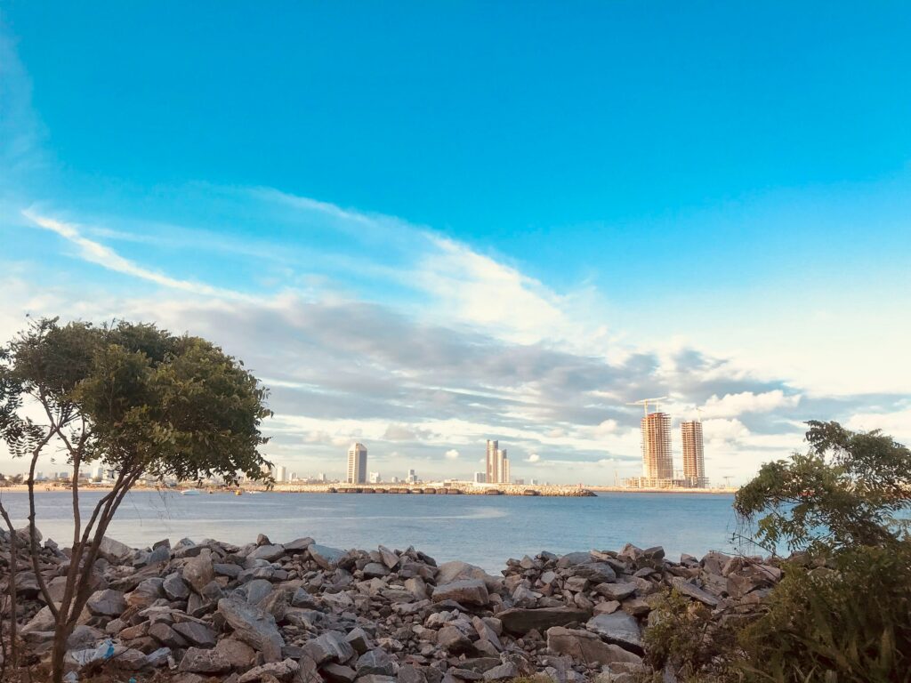 Vista da Tarkwa Bay, Lagos, Nigéria durante o dia, com uma árvore do lado esquerdo em frente um mar e ao fundo os prédios. Representa chip internacional para a Nigéria.

