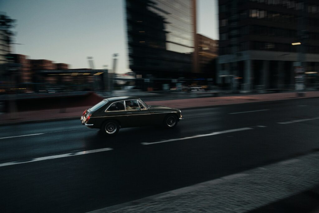 Um carro antigo passa rapidamente por uma rua na Alemanha ao anoitecer, com prédios desfocados ao fundo. Representa aluguel de carros na Alemanha.