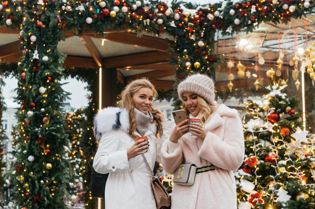 Duas mulheres com casacos de inverno estão em uma área festiva e decorada, segurando bebidas quentes e sorrindo, em Moscou, Rússia.