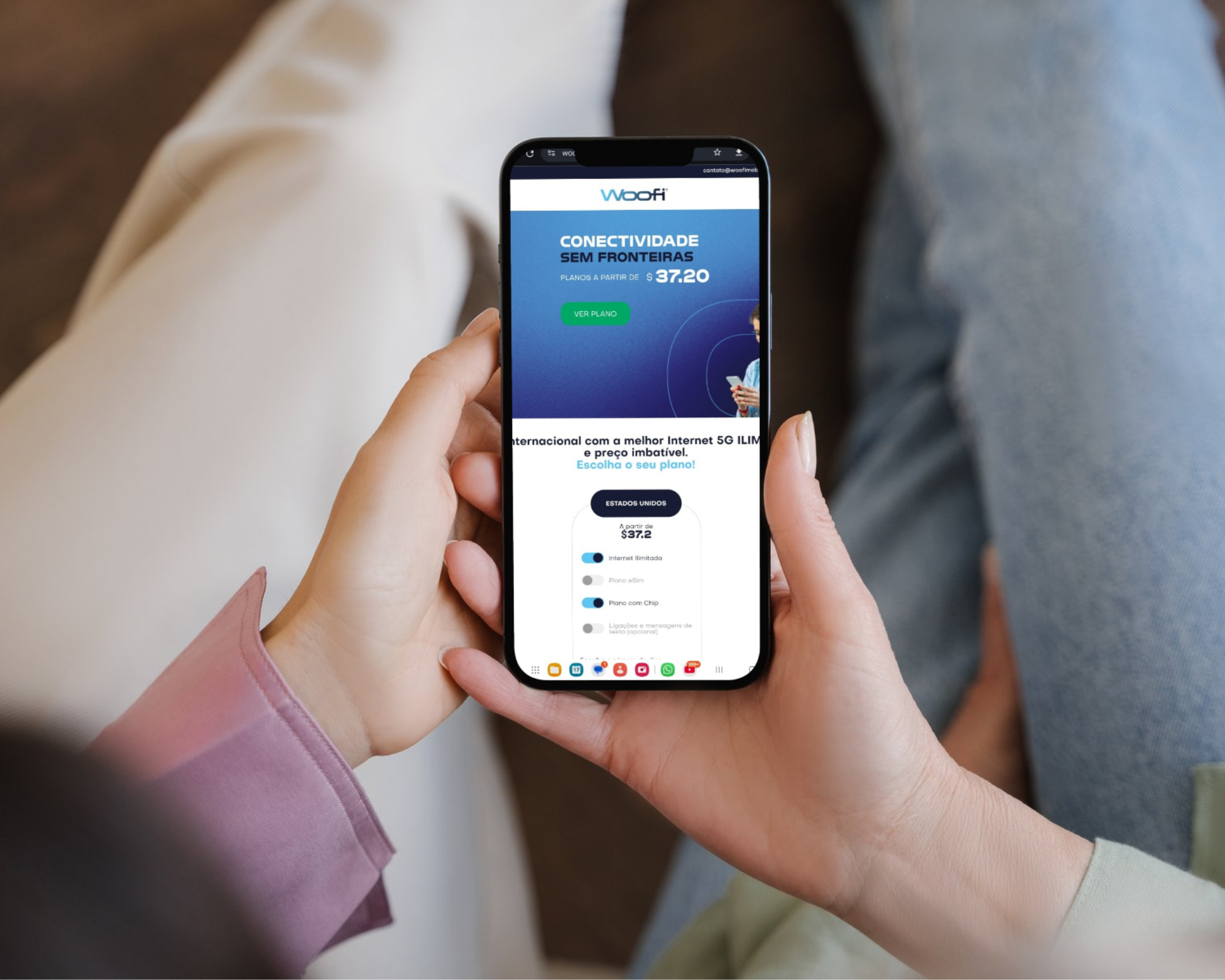 Pessoa segurando um smartphone exibindo o site da Woofi com elementos de design em azul e branco.