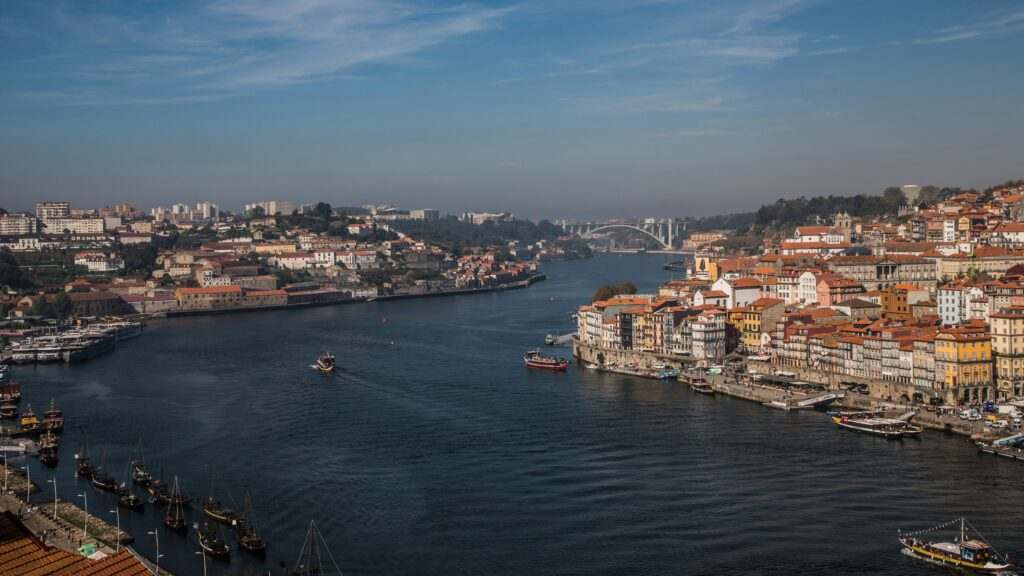 Vista de um rio correndo por Porto com pontes, barcos e edifícios à beira-mar sob um céu limpo. Representa chip internacional para o Porto.