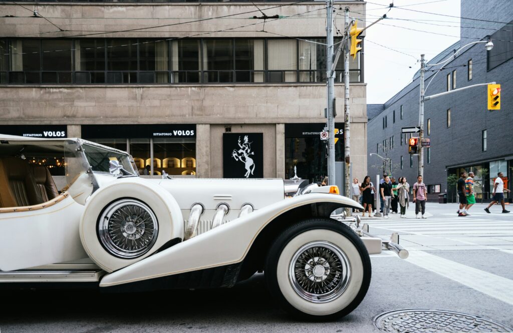 Um carro branco antigo estacionado em uma rua de Toronto com prédios e pedestres ao fundo. Representa aluguel de carros no Canadá.