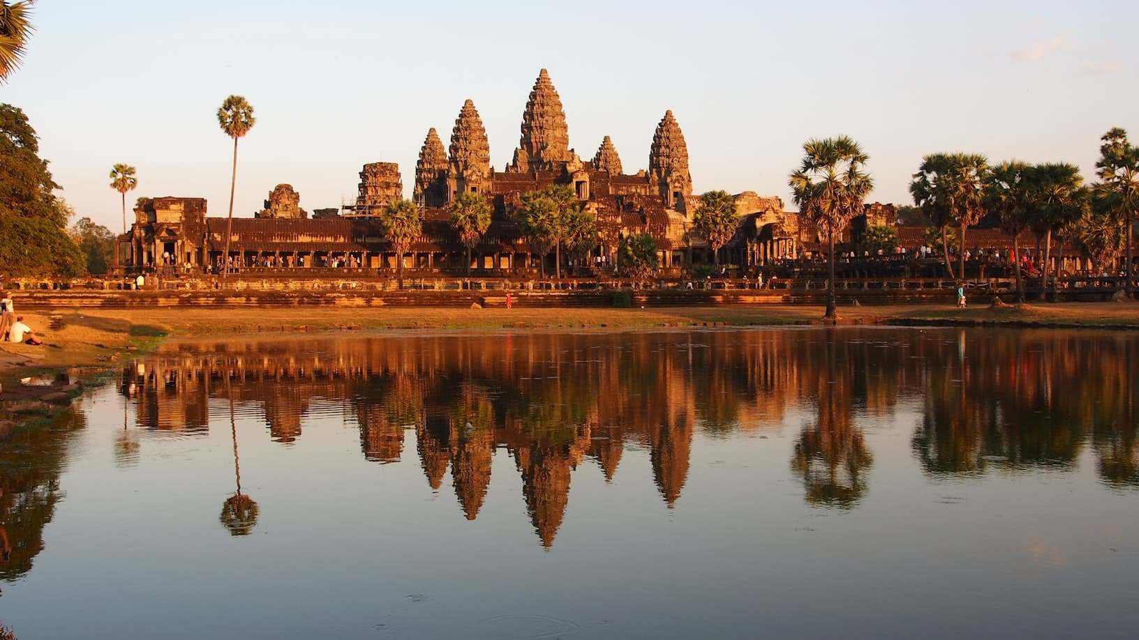 Complexo de templos de Angkor Wat no Camboja refletido em um lago calmo ao pôr do sol, com palmeiras ao redor da área. Representa eSIM Camboja.