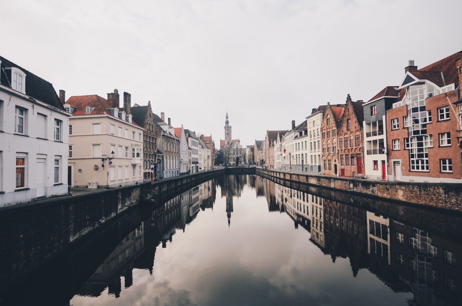 Um canal ladeado por edifícios tradicionais europeus em Brugge que reflete o céu nublado e a arquitetura em uma composição calma e simétrica. Representa eSIM Bélgica.
