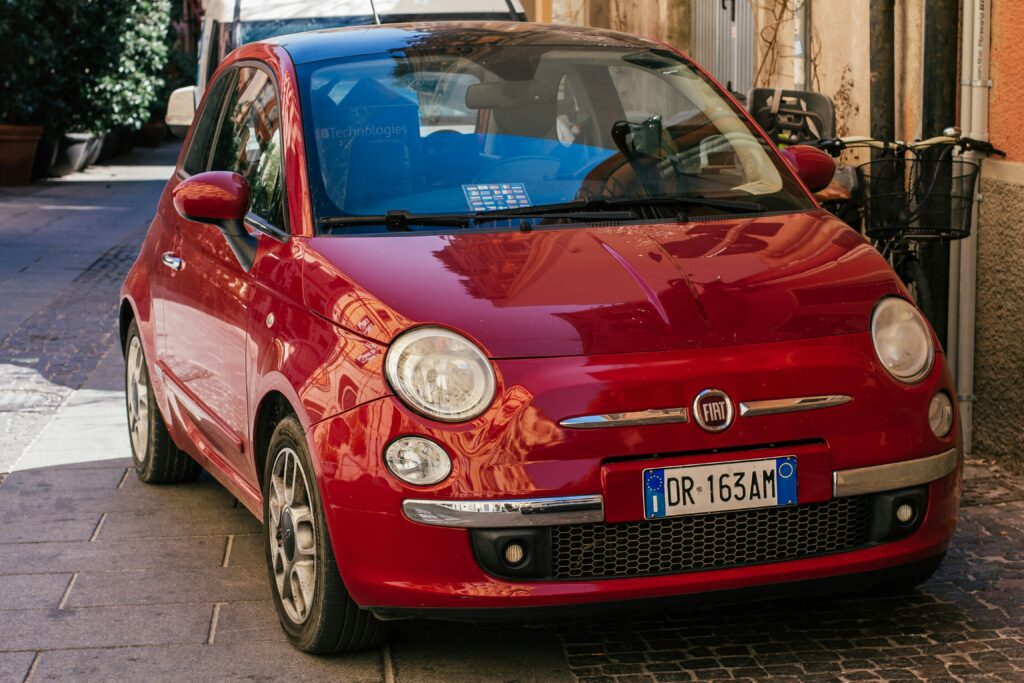 Um Fiat 500 vermelho está estacionado em uma rua estreita com calçamento de paralelepípedos, em Cagliari. Representa aluguel de carros na Itália