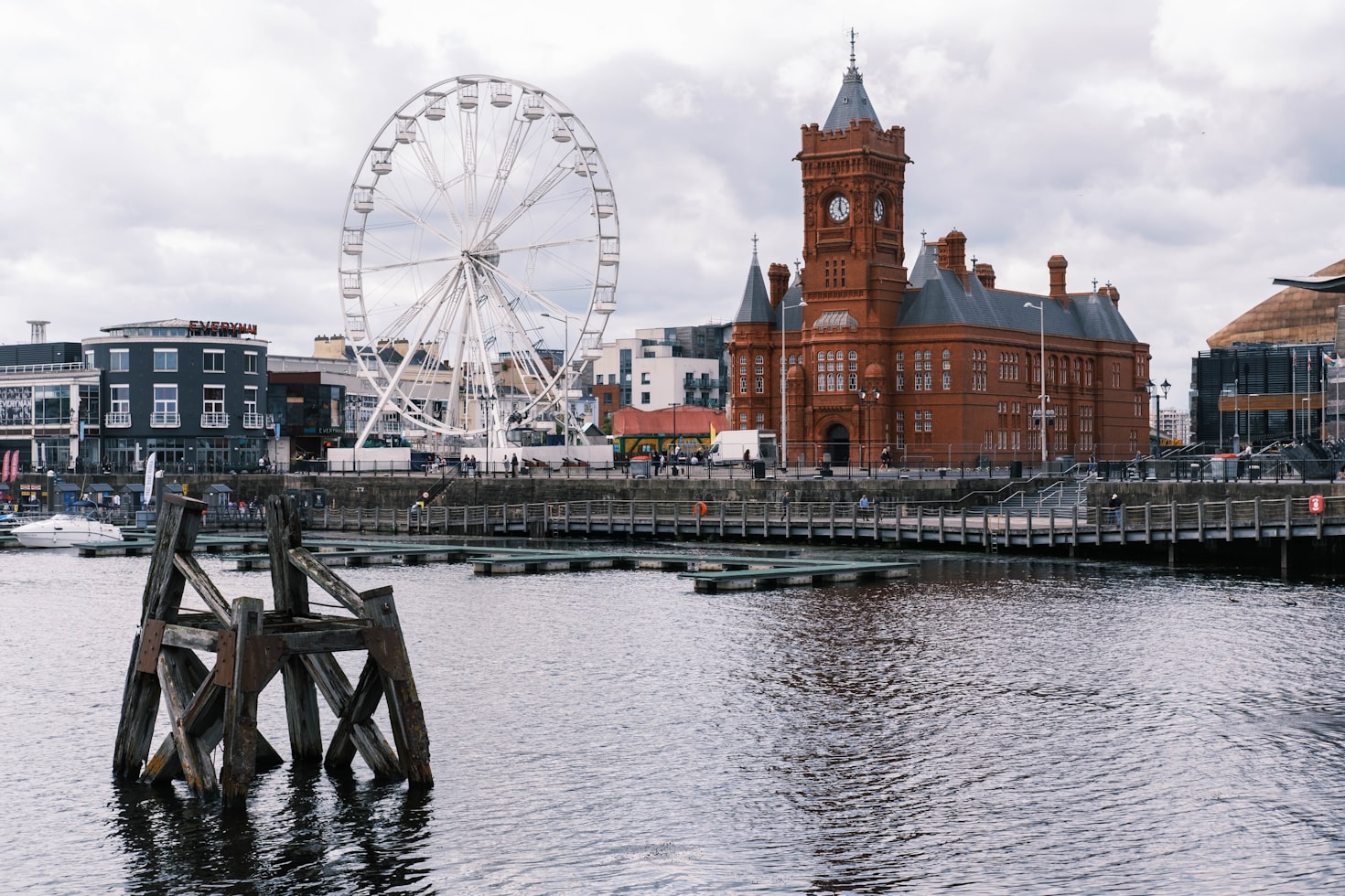 Uma cena à beira-mar da Cardiff Bay com uma torre de relógio de tijolos vermelhos, uma roda-gigante e vários edifícios modernos sob um céu nublado. Representa eSIM País de Gales.