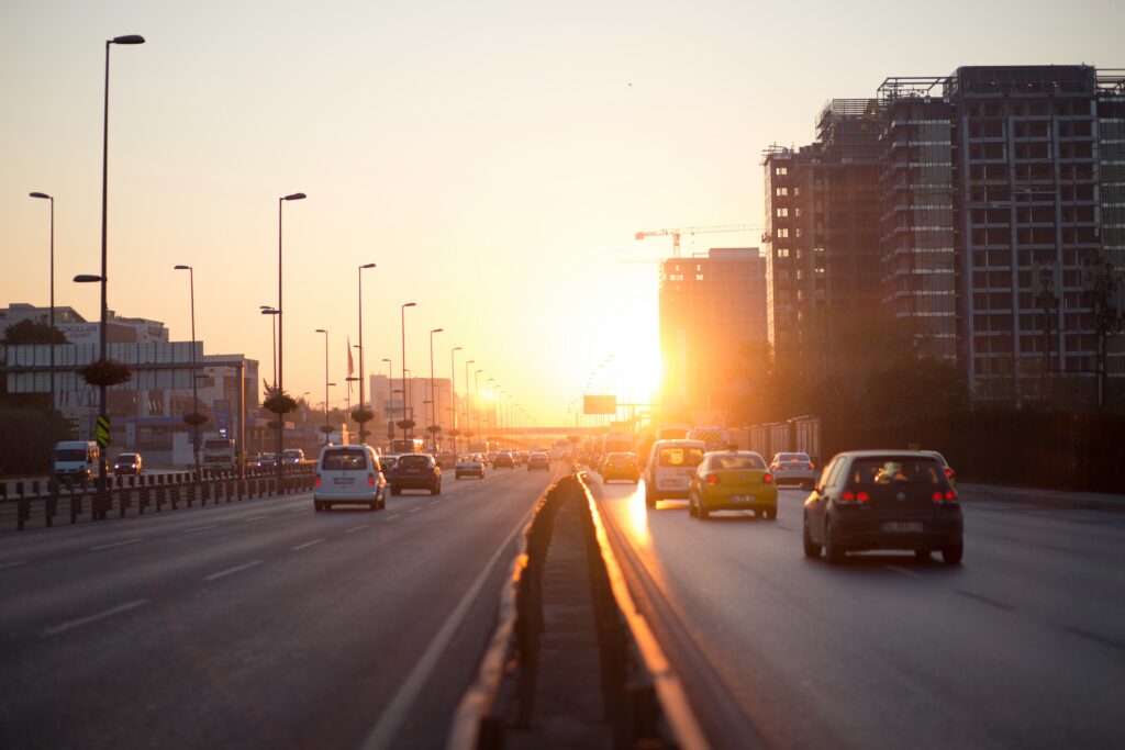Carros dirigindo em uma rodovia em Istambul de várias faixas durante o pôr do sol, com prédios e um guindaste de construção ao fundo.