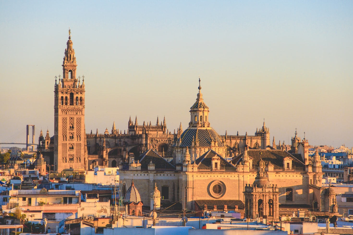 Uma vista da paisagem urbana mostrando a Catedral de Sevilha e a torre do sino La Giralda sob um céu claro ao pôr do sol, com edifícios ao redor. Representa eSIM Espanha.