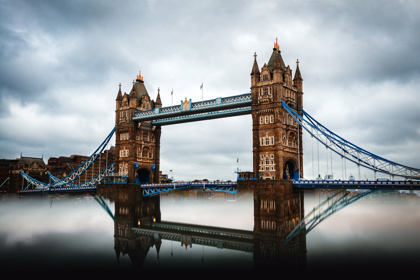 A imagem mostra a Tower Bridge em Londres com suas duas torres e basculantes refletidas em um rio calmo sob um céu nublado. Representa eSIM Inglaterra.