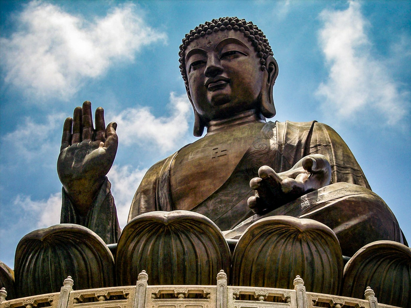Grande estátua de Buda de bronze contra um céu azul com nuvens, com uma mão levantada e a outra apoiada no colo, em Lantau Island. Representa eSIM Hong Kong.