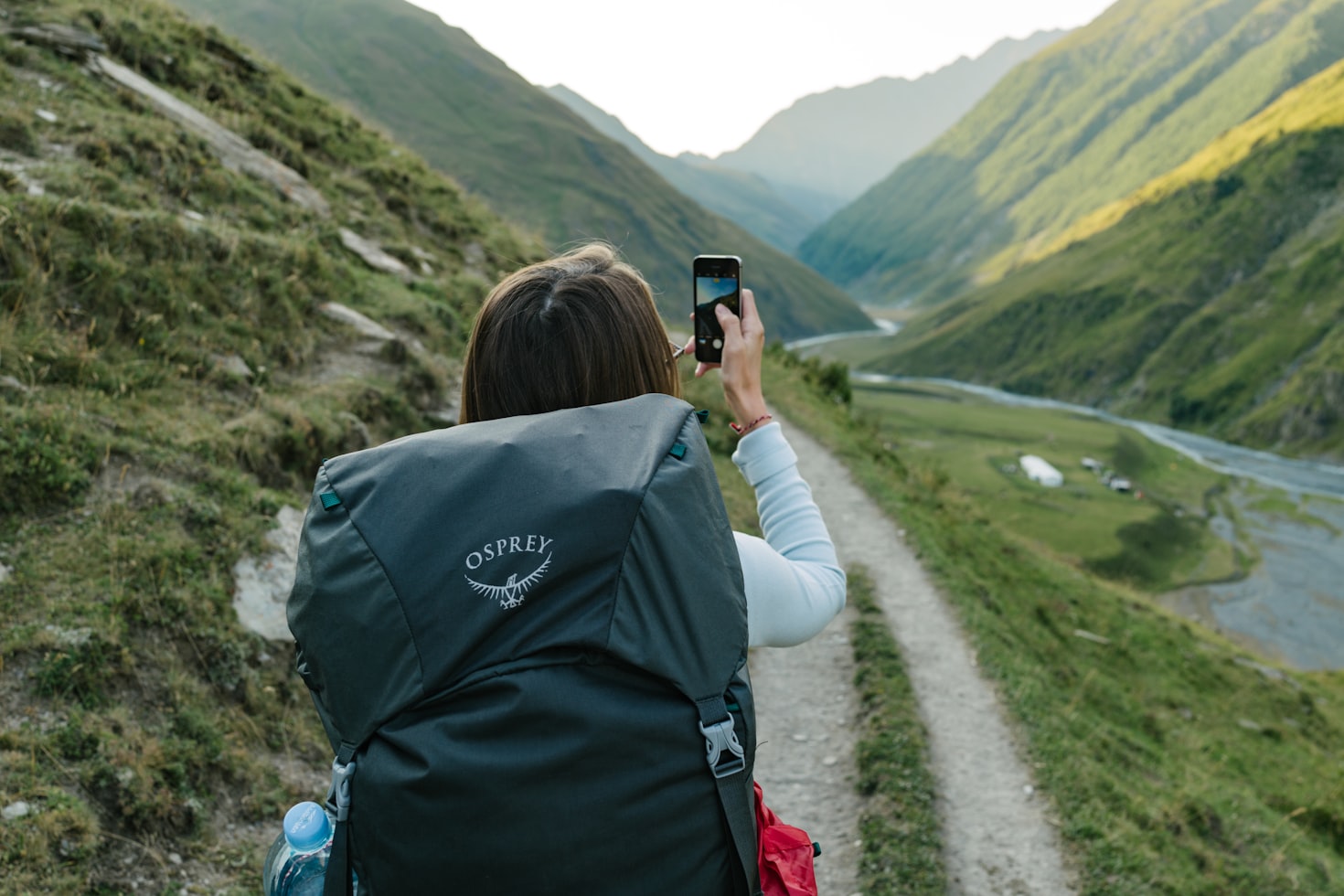 Uma pessoa com uma mochila tira uma foto de um vale e montanhas em Cordilheira do Cáucaso em um dia claro.