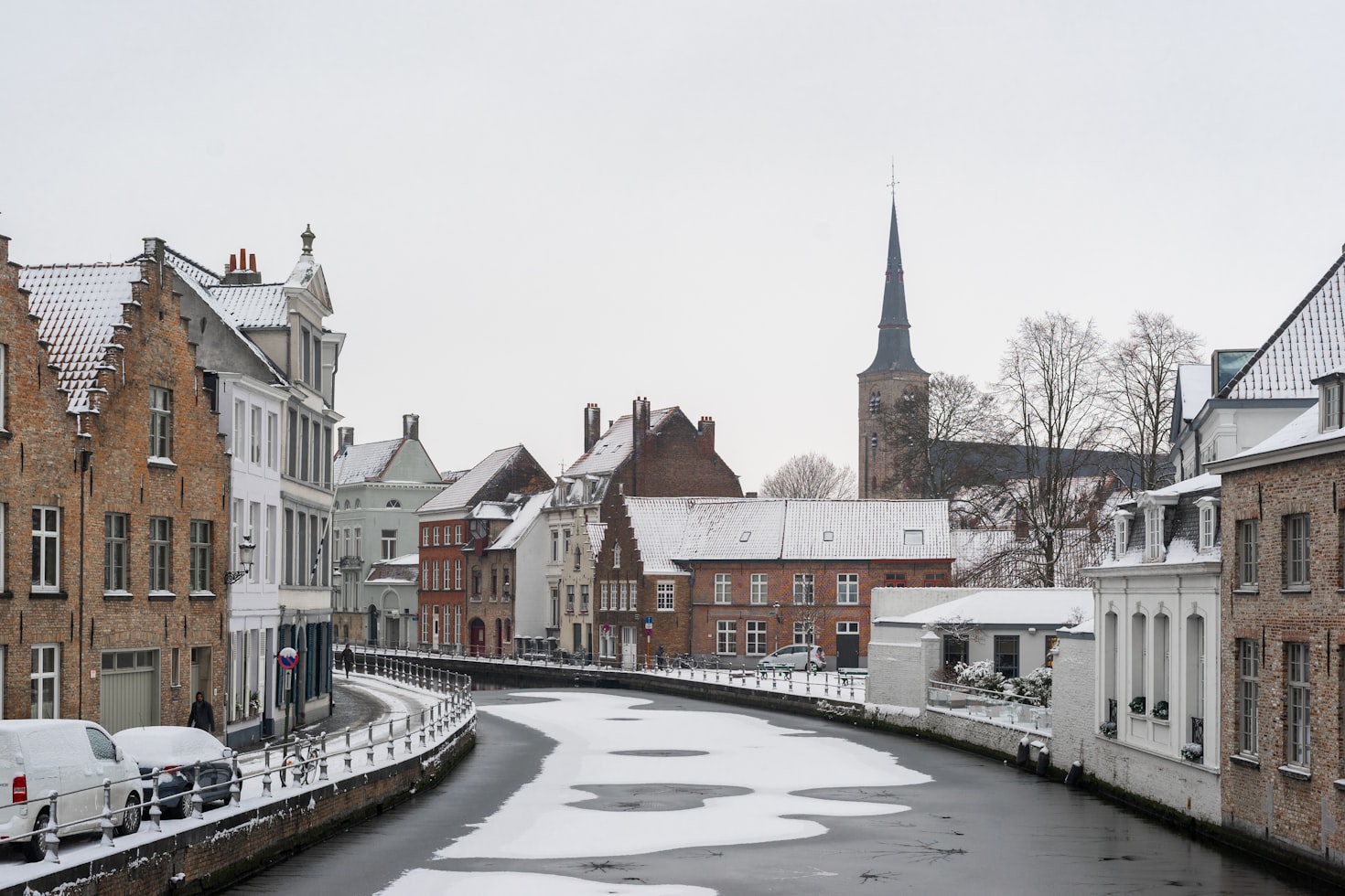 Canal coberto de neve com água parcialmente congelada, cercado por edifícios históricos e uma torre de igreja em Brugge. Representa eSIM Bélgica.