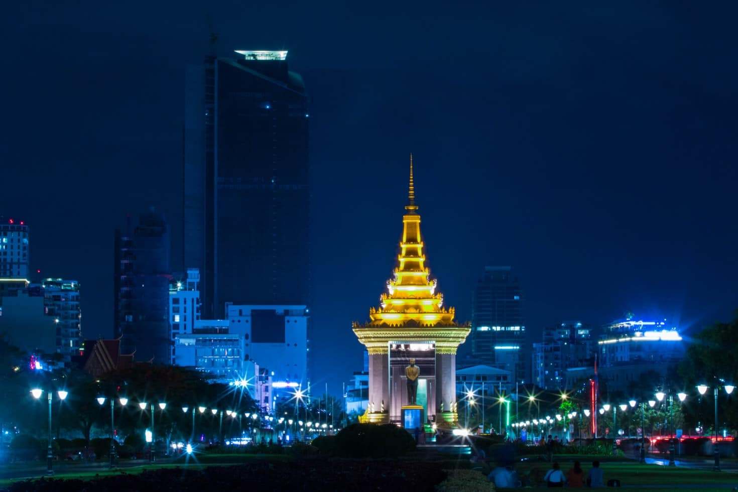 Monumento dourado iluminado à noite com prédios da cidade ao fundo, cercado por um parque e luzes do caminho, em Phnom Penh. Representa eSIM Camboja.