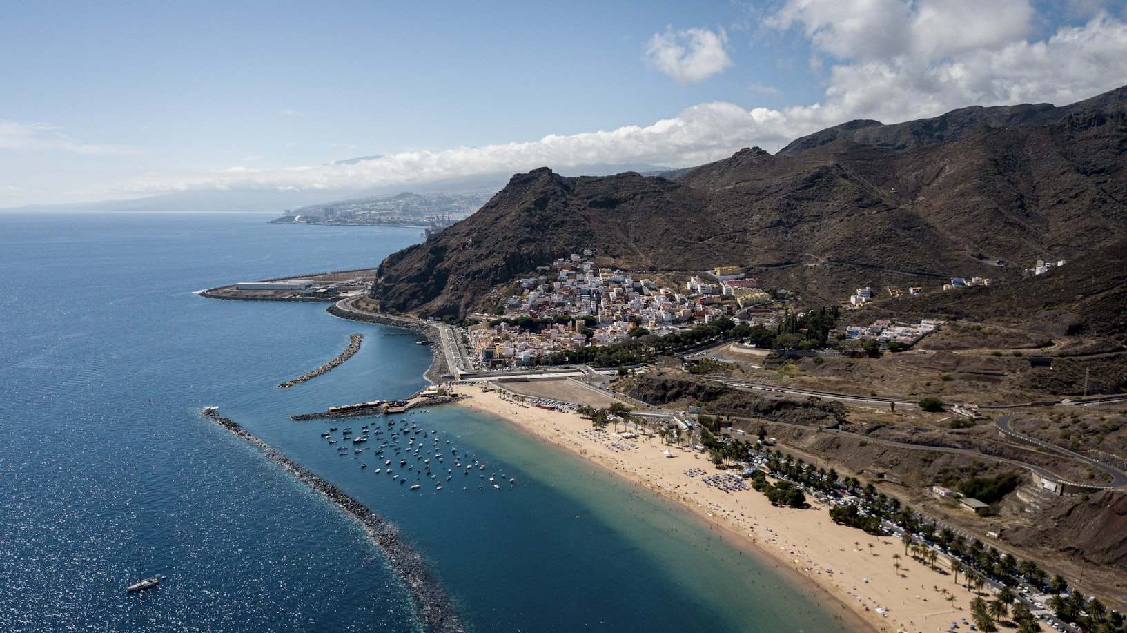 Vista aérea de uma área costeira de San Andrés com uma praia de areia, montanhas, pequenos barcos na água e edifícios espalhados perto da costa. Representa eSIM San Andrés.