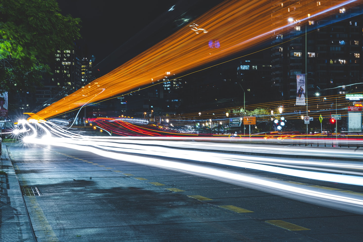 Foto noturna de longa exposição de uma rua da cidade, com rastros de luz branca e laranja borrados de veículos contra um cenário urbano, em Santiago.