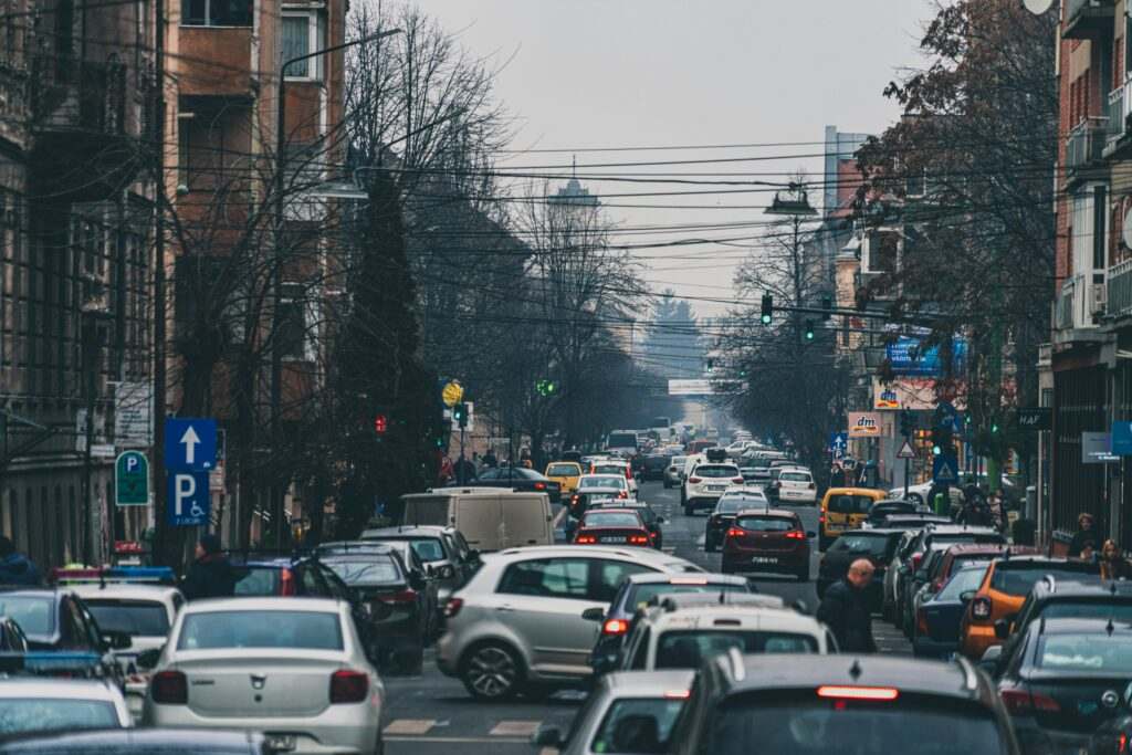 Uma rua de Arad na Romênia movimentada com tráfego pesado e carros estacionados. Pessoas e veículos preenchem a cena sob um céu nublado. Representa aluguel de carros em Lisboa.