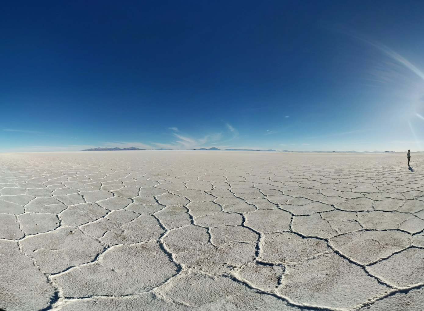 Vasta paisagem de salina sob um céu azul claro com uma pessoa à distância no lado direito, na Bolívia. Representa eSIM América do Sul.