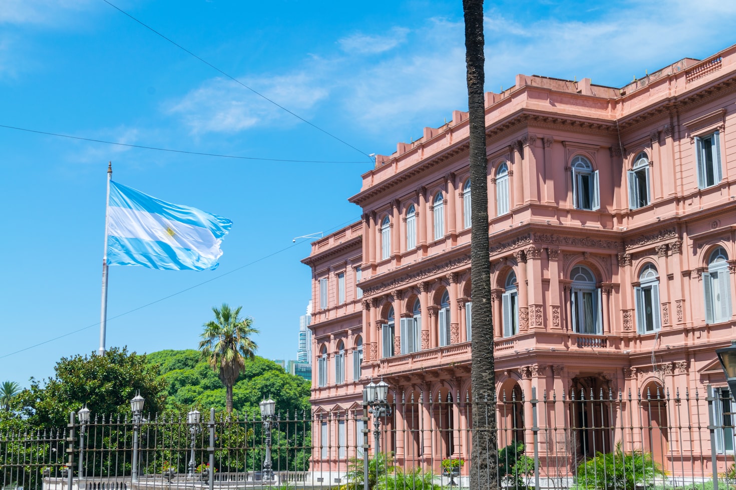 A imagem mostra a Casa Rosada rosa em Buenos Aires com a bandeira argentina tremulando sob um céu azul. Representa eSIM Argentina.
