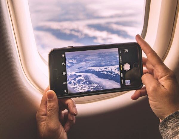 Uma pessoa tira uma foto das nuvens e montanhas através da janela de um avião usando um smartphone.