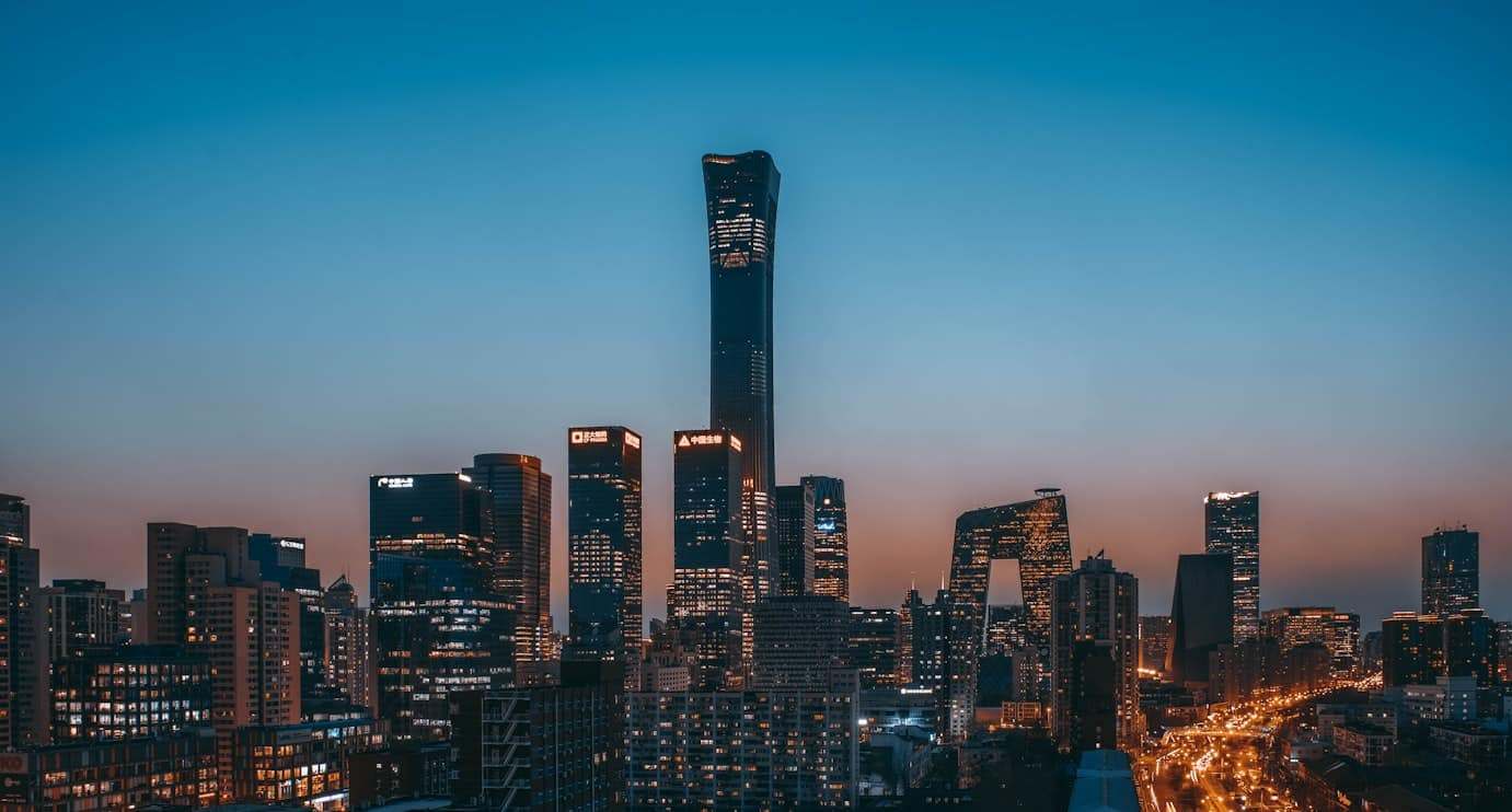 Horizonte de Pequim ao anoitecer, com arranha-céus altos e iluminados, com um edifício proeminente no centro, sob um céu claro à noite.