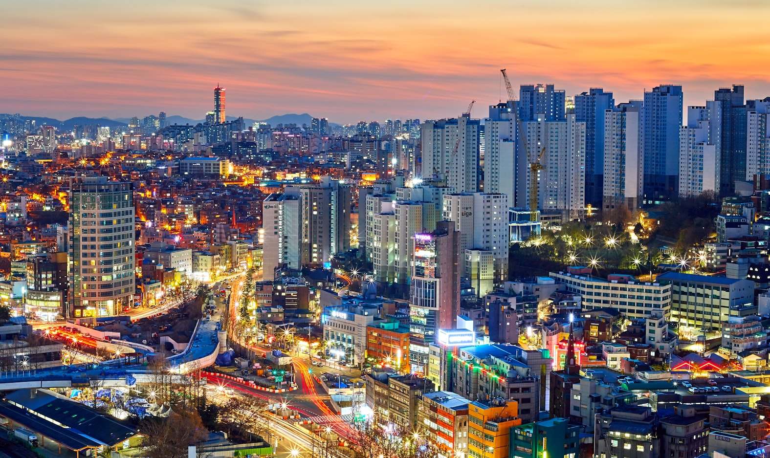 Horizonte de Seoul, ao anoitecer com prédios altos, luzes coloridas e ruas movimentadas. O céu está laranja e azul, indicando o pôr do sol, em Seoul. Representa eSIM Coreia do Sul.