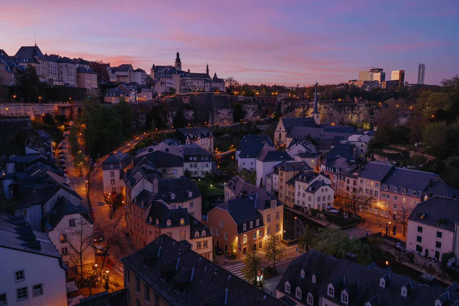 Uma paisagem urbana noturna mostra a cidade de Luxemburgo no topo de uma colina sob um céu roxo, com ruas iluminadas e edifícios de estilo histórico. Representa eSIM Luxemburgo.