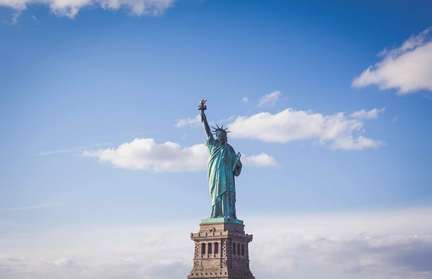 A Estátua da Liberdade fica em um pedestal contra um céu azul com nuvens dispersas. Representa eSIM Nova York.