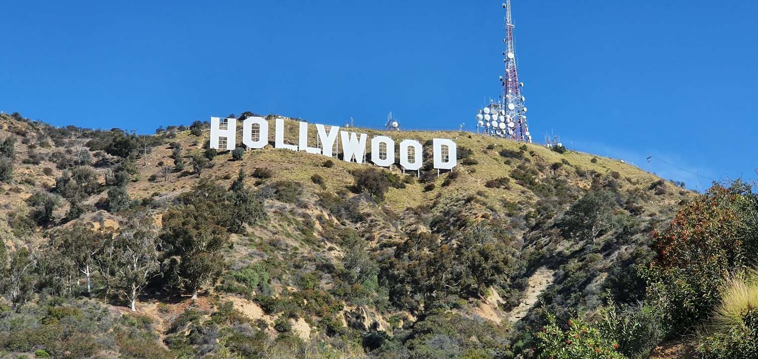 O letreiro de Hollywood em uma encosta com um céu azul claro e uma alta torre de comunicação ao fundo. Representa eSIM Los Angeles.