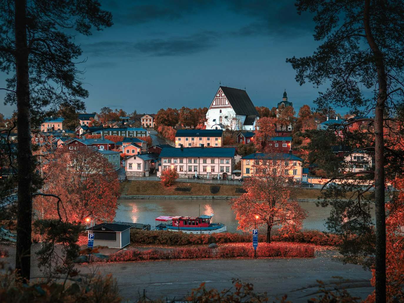 Pequena cidade de Old Porvoo com prédios coloridos e uma igreja perto de um rio, cercada por árvores. Um barco vermelho está na água, sob um céu nublado. Representa eSIM Finlândia.
