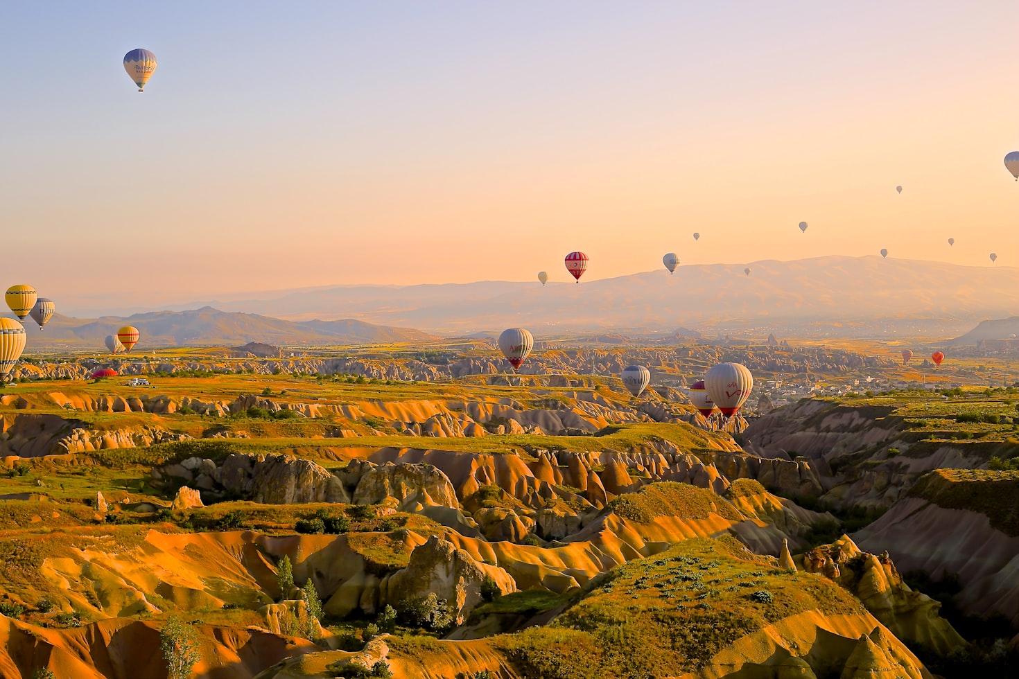 Balões de ar quente flutuam sobre uma paisagem de colinas e formações rochosas ao nascer do sol, sob um céu claro, na Capadócia. Representa eSIM Capadócia.