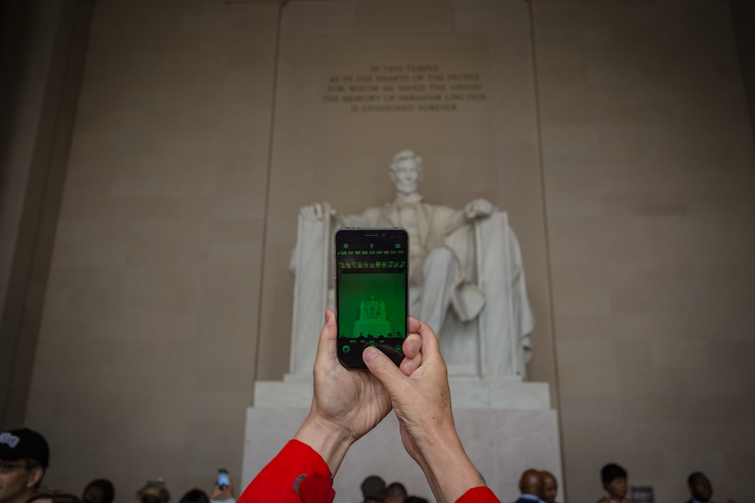 Pessoa de vermelho segura o telefone, fotografando a estátua do Lincoln Memorial dentro de um grande salão, com várias pessoas ao fundo. Representa chip internacional.