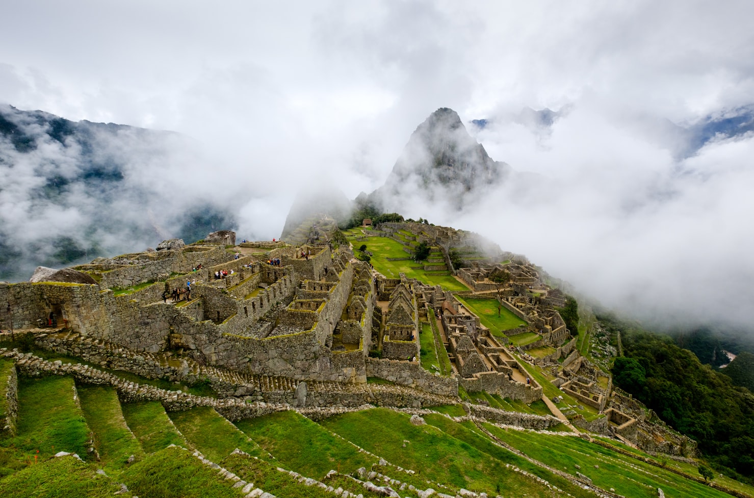 Vista aérea de Machu Picchu com ruínas de pedra e terraços verdes cercados por montanhas cobertas de névoa e nuvens. Representa eSIM Machu Picchu.