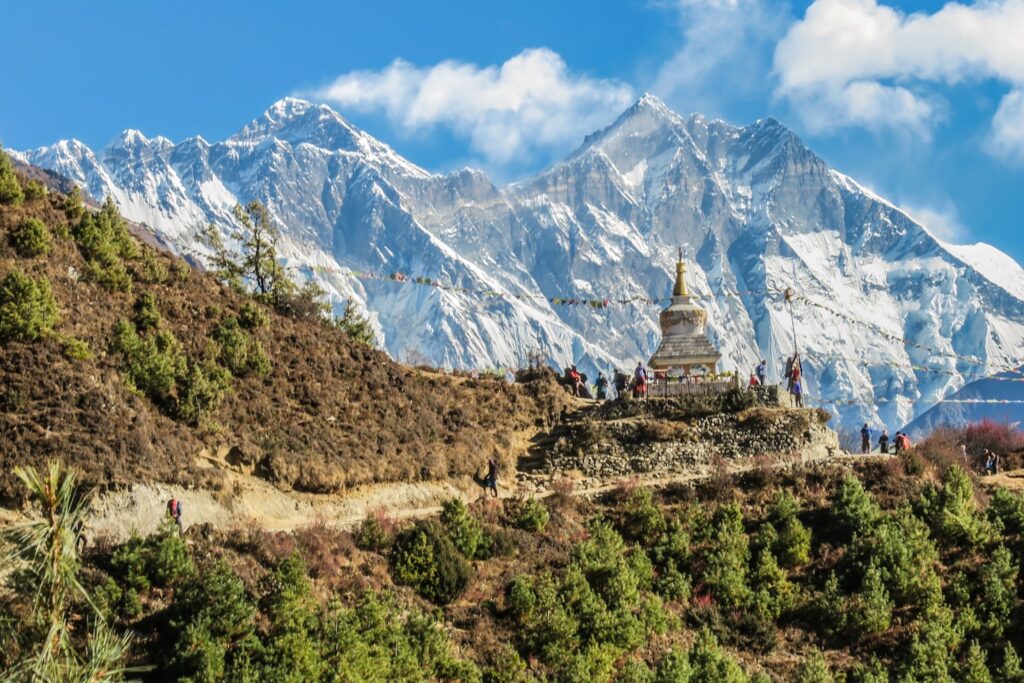 Um stupa fica em uma colina com bandeiras de oração, cercado por árvores e com montanhas cobertas de neve ao fundo, no Nepal.