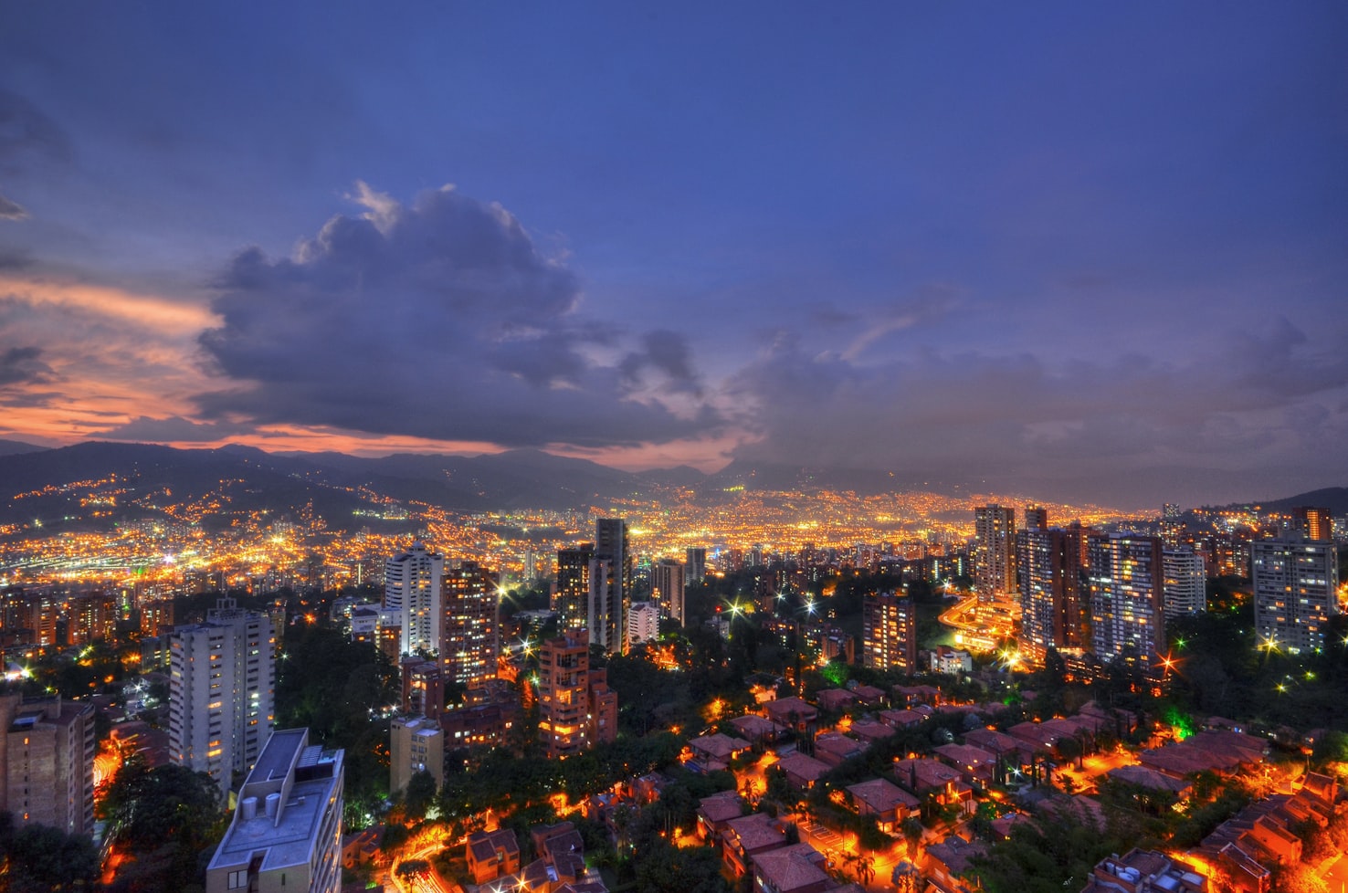 Paisagem urbana de Medellín ao entardecer com prédios, ruas iluminadas e montanhas ao fundo sob um céu nublado. Representa eSIM Medellín.