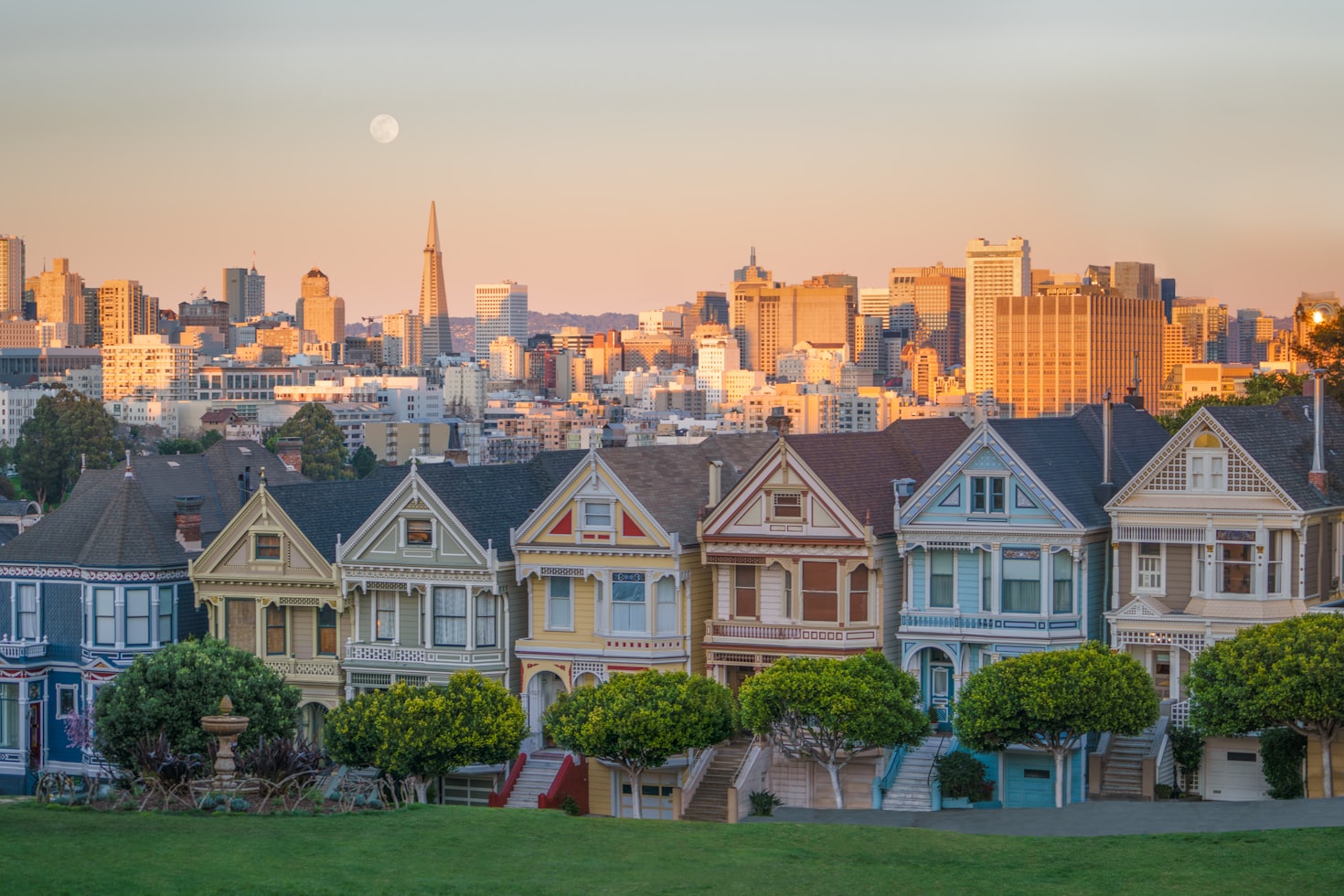 Casas vitorianas, conhecidas como Painted Ladies, com o horizonte de São Francisco e uma lua ao fundo ao pôr do sol. Representa eSIM San Francisco.