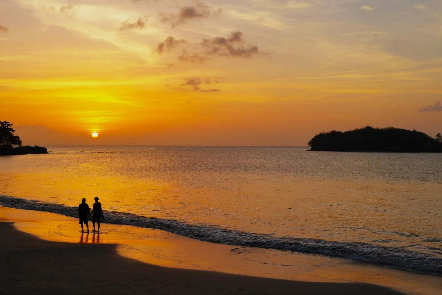 Duas pessoas estão em uma praia ao pôr do sol, olhando para o oceano com uma ilha e nuvens ao longe, em Santa Lúcia. Representa eSIM Santa Lúcia.