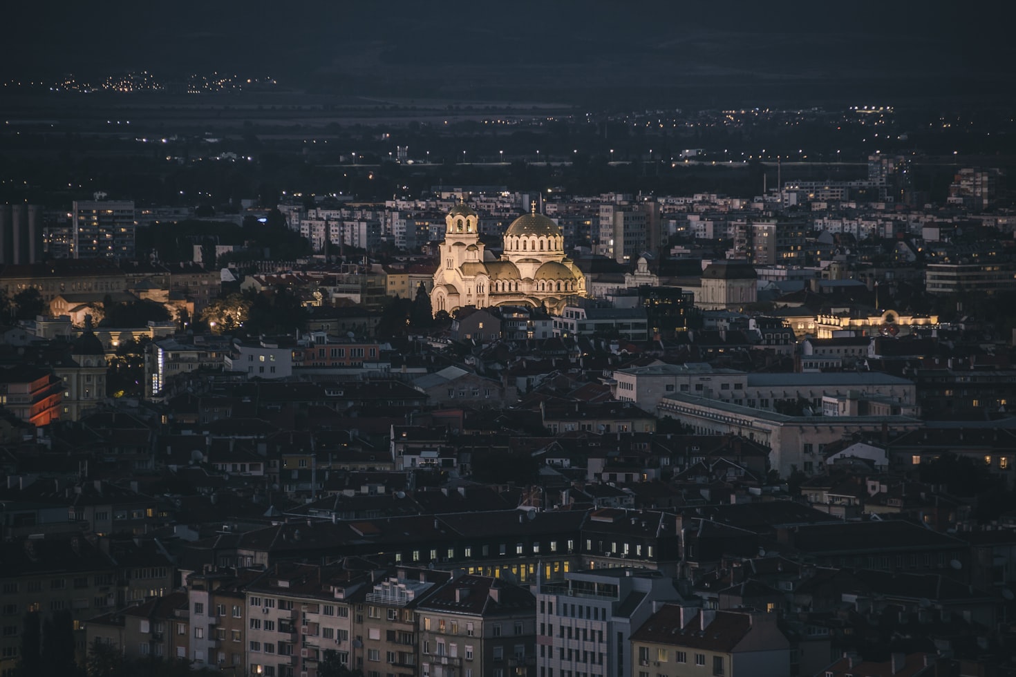 Vista aérea noturna da cidade Sofia com uma grande catedral iluminada no centro. Prédios ao redor aparecem sob um céu escuro. Representa eSIM Bulgária.