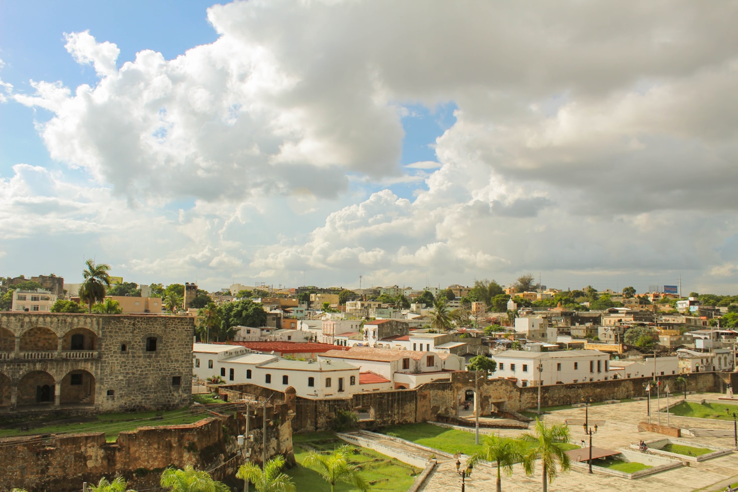 Vista de uma área histórica da cidade com antigos edifícios de pedra, casas brancas, grama verde e céu nublado ,na República Dominicana. Representa eSIM República Dominicana.