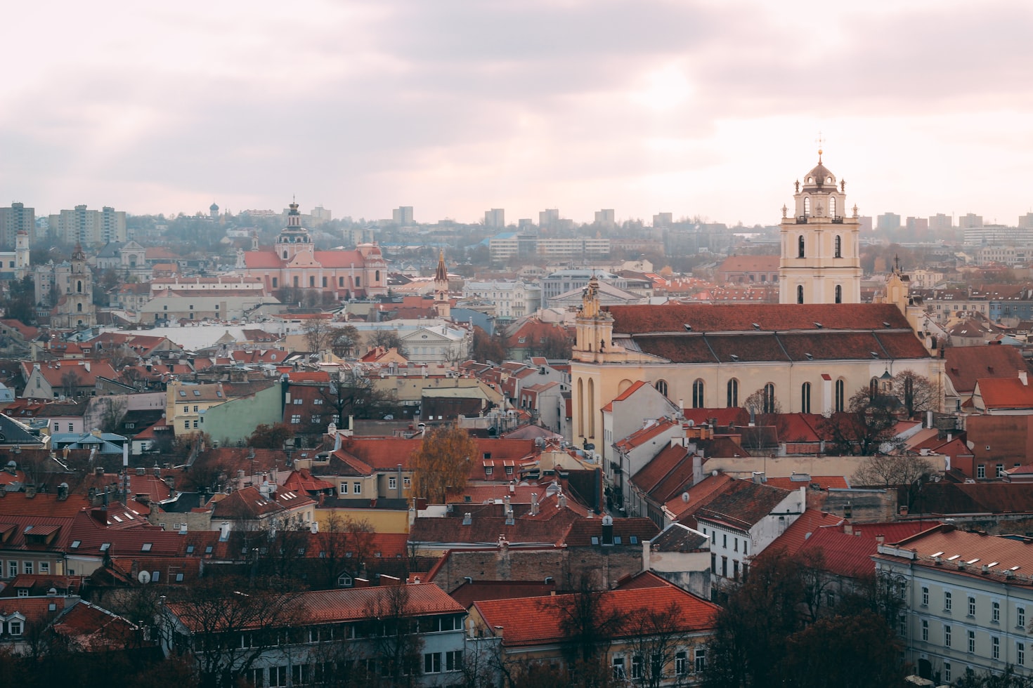 Vista aérea de uma paisagem urbana de Vilnius com prédios com telhados vermelhos, torres de igrejas e um cenário de arranha-céus modernos sob um céu nublado. Representa eSIM Lituânia.
