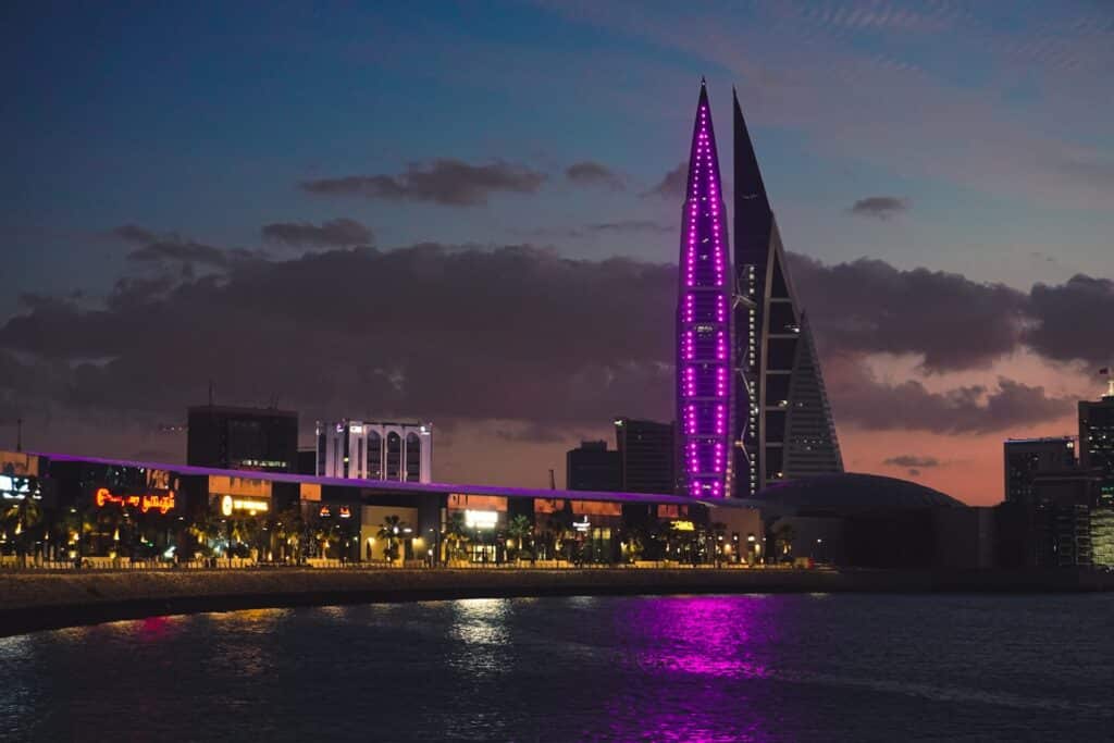 Horizonte da cidade ao entardecer com orla, prédios altos e luzes rosas refletindo na água, em Bahrain. Representa eSIM Bahrein.