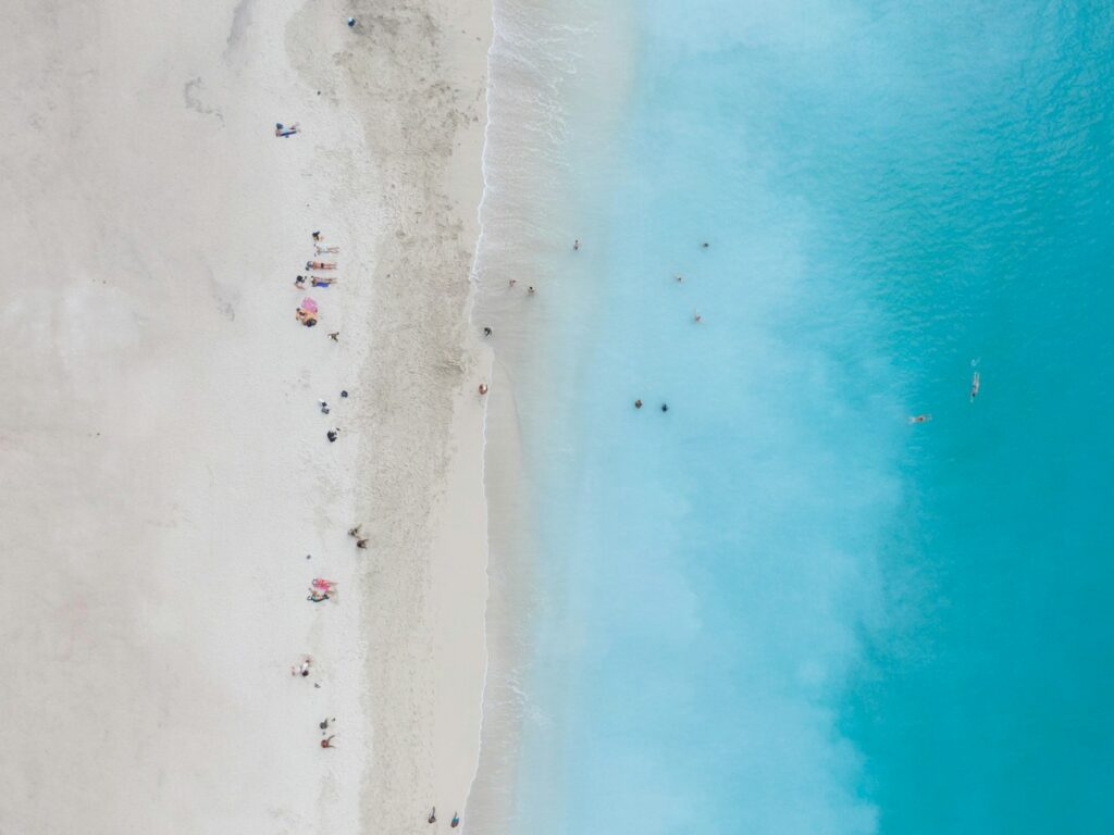 Vista aérea de uma praia de areia com pessoas na praia e outras nadando em águas azuis cristalinas, em Mindelo. Representa eSIM Cabo Verde.
